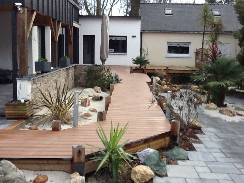 Allée de jardin en composite gris-brun - Luc Rautureau (85) Aménagement extérieur avec une allée en lames de composite surélevée qui serpente à travers un jardin paysager sec.