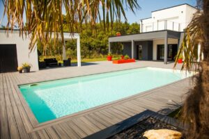 Grande terrasse moderne en composite gris entourant une piscine rectangulaire au pied d'une maison d'architecte blanche.