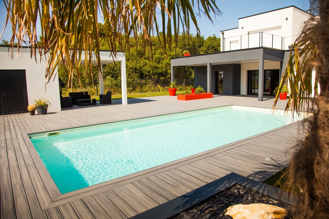 Grande terrasse moderne en composite gris entourant une piscine rectangulaire au pied d'une maison d'architecte blanche.