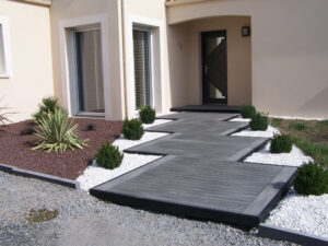 Chemin d'entrée de maison en bois composite gris foncé. Habillage de cailloux blanc pour faire ressortir la couleur du bois.