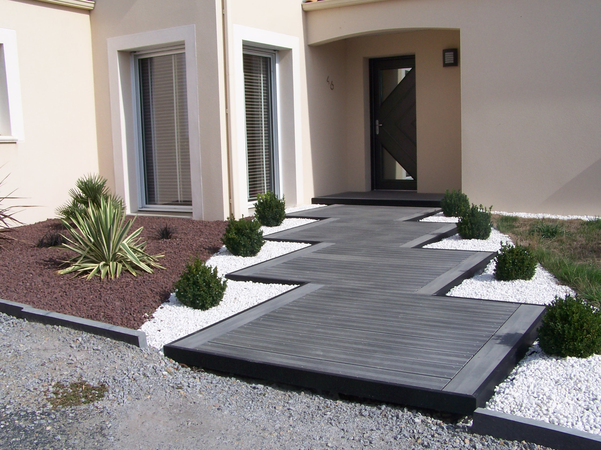 Chemin d'entrée de maison en bois composite gris foncé. Habillage de cailloux blanc pour faire ressortir la couleur du bois.
