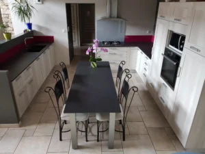 Aménagement de cuisine ouverte avec grand plan de travail noir, crédence fuchsia et table centrale.