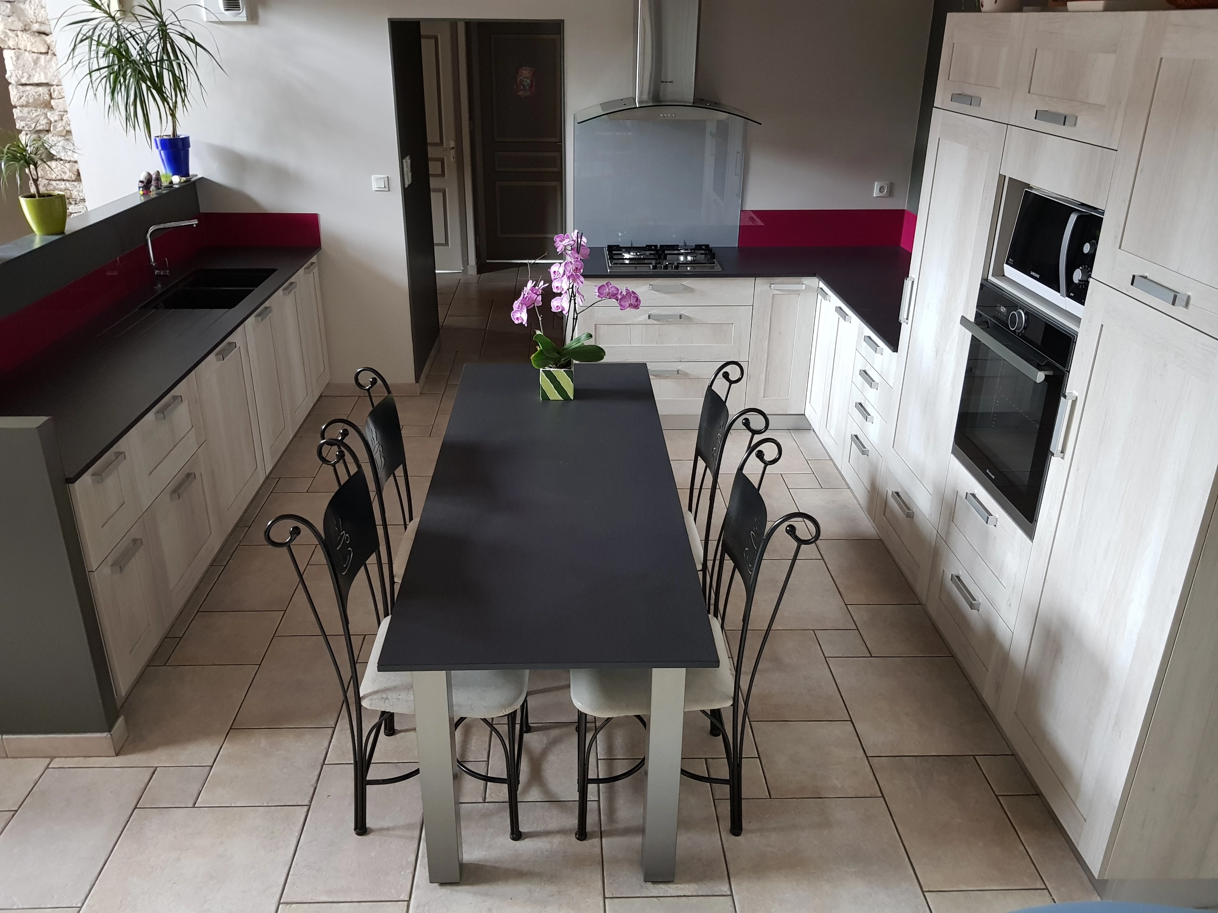 Aménagement de cuisine ouverte avec grand plan de travail noir, crédence fuchsia et table centrale.