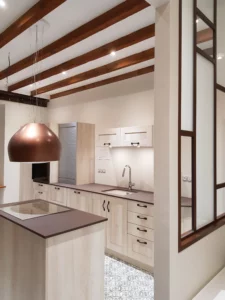 Cuisine moderne en bois clair avec plan de travail foncé, hotte design cuivrée et poutres en bois.