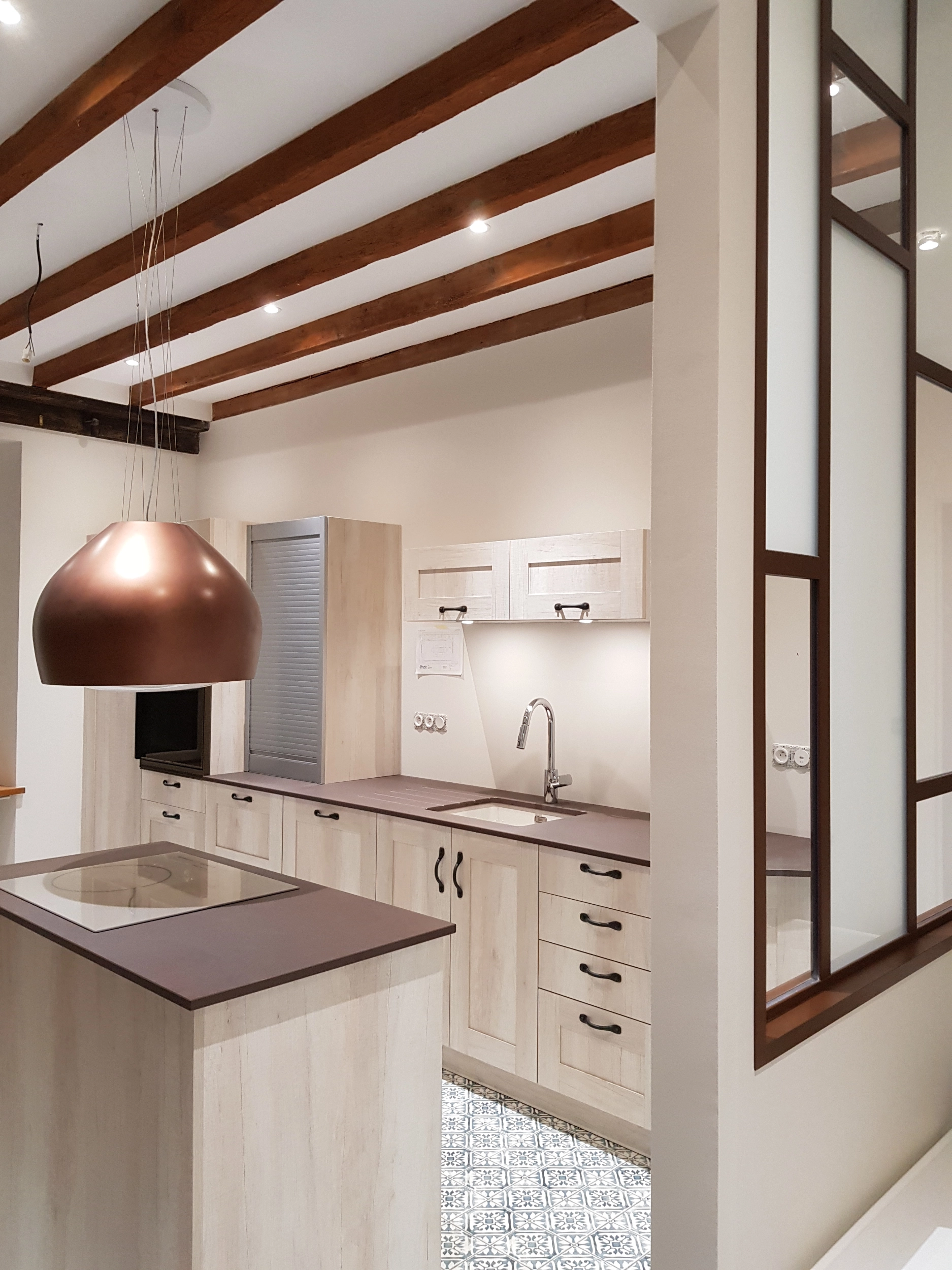 Cuisine moderne en bois clair avec plan de travail foncé, hotte design cuivrée et poutres en bois.