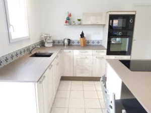 Aménagement de cuisine en L en bois clair et crédence carreaux de ciment.
