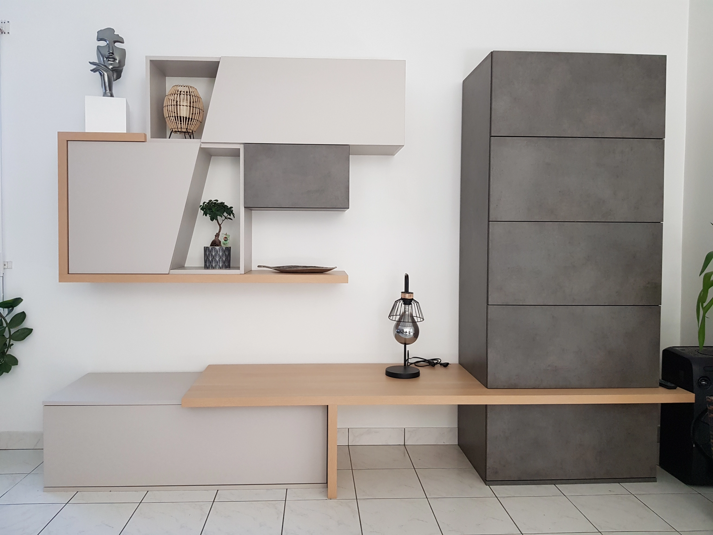Ensemble de mobilier de salon avec des blocs de rangement muraux suspendus gris et beige, une étagère en bois clair et une lampe design posée sur le plateau.