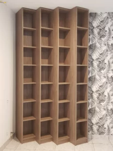 Étagère bibliothèque verticale sur mesure en bois clair à quatre colonnes, installée à côté d'un mur habillé d'un papier peint à motifs de feuillage noir et blanc.