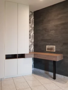 Espace de travail avec un bureau suspendu en bois sans pieds, adossé à un grand placard blanc minimaliste et un mur en plaquettes de parement en ardoise noire.