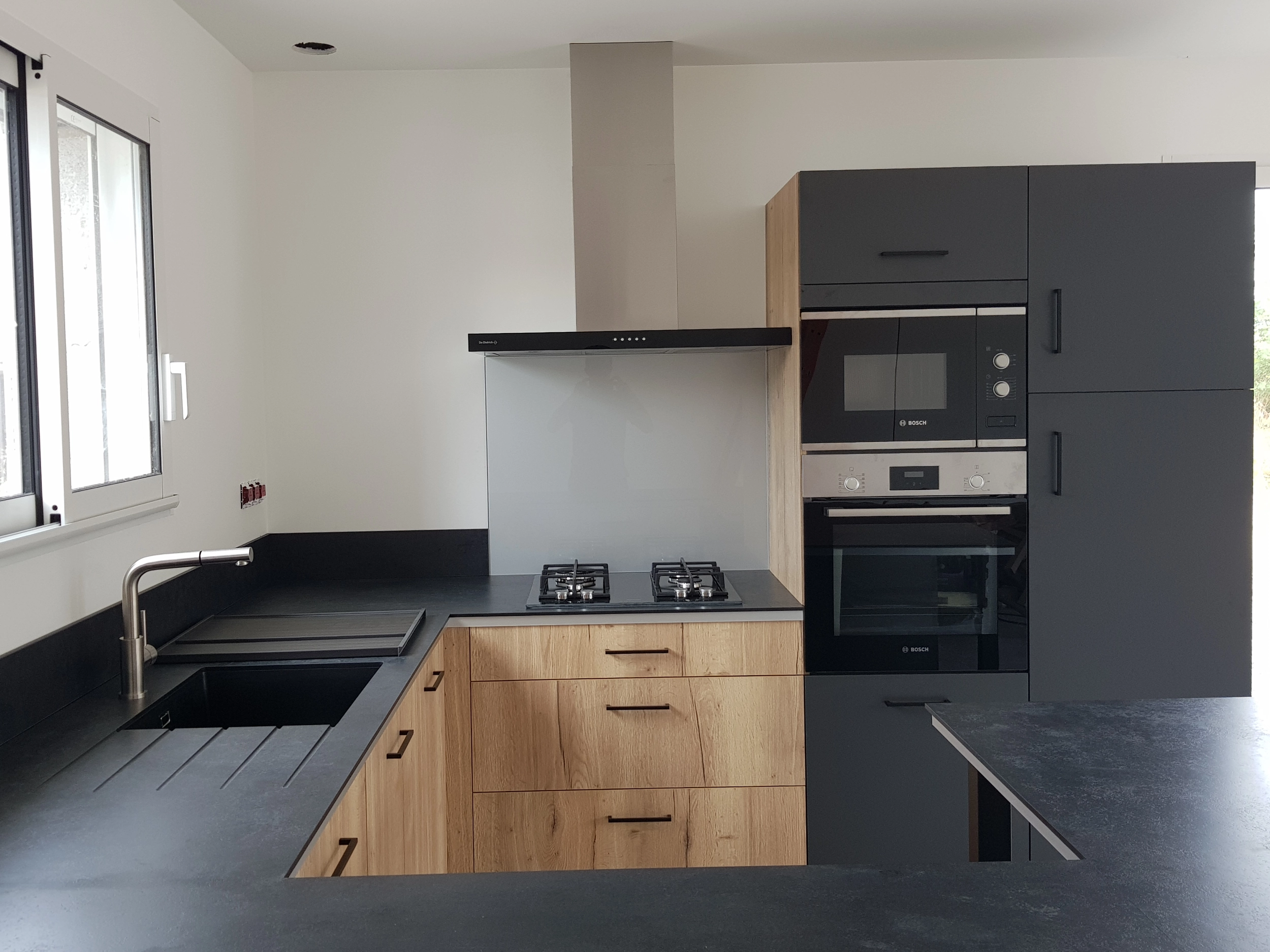 Cuisine moderne de couleur noir pour le plan de travail et certaines façades de placard. Un mélange de façade bois pour contraster et donner le côté moderne de cette cuisine