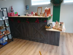 Comptoir de caisse en bois foncé avec motifs en X, décoré d'une guirlande de sapin et de nœuds rouges pour les fêtes de Noël, installé dans un institut ou une boutique.