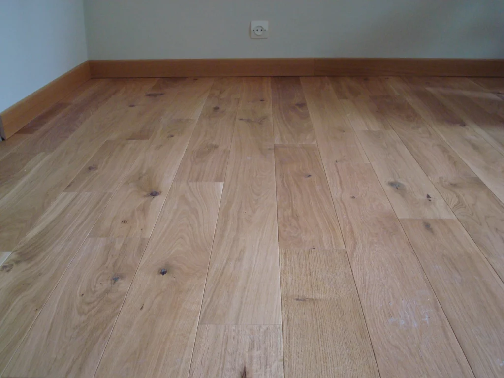 Pose de parquet en chêne massif - Luc Rautureau (85) Zoom au sol sur un parquet en chêne véritable avec plinthes assorties, posé dans une pièce lumineuse.