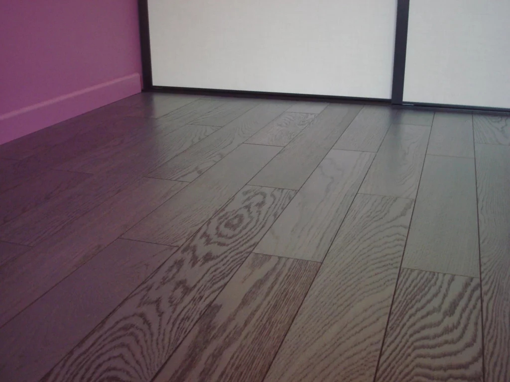 Parquet teinté contemporain - Luc Rautureau (85) Parquet en bois teinté gris foncé à larges lames avec plinthe assortie au pied d'un mur violet.