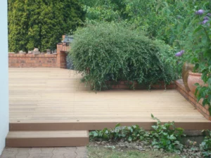 Marches d'une terrasse en bois naturel clair bordée par un muret de briques rouges surmonté de verdure.