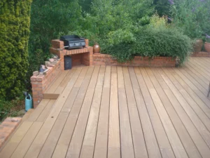 Vue de dessus d'une terrasse en lames de bois avec une structure de barbecue intégrée dans un muret en briques rouges.