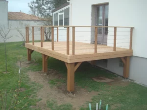 Terrasse en bois clair surélevée sur poteaux, sécurisée par un garde-corps moderne avec des câbles en inox.