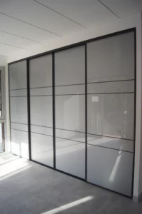 Grande cloison de placard à quatre portes coulissantes en verre dépoli et profilés noirs au design contemporain.