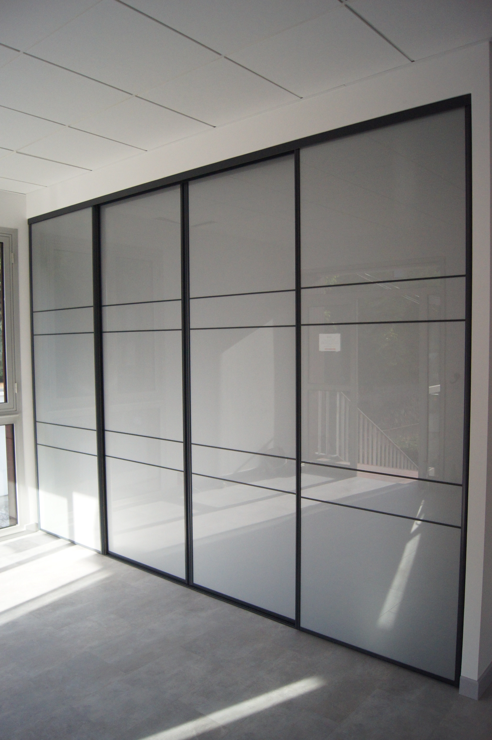 Grande cloison de placard à quatre portes coulissantes en verre dépoli et profilés noirs au design contemporain.