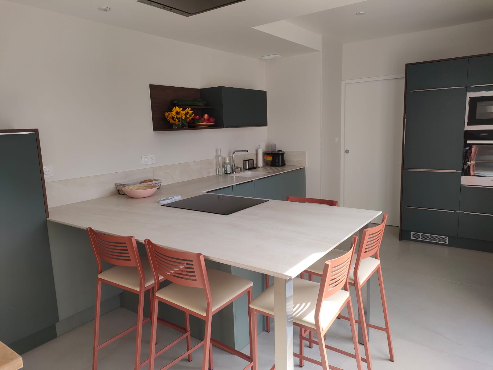 Cuisine moderne avec un plan de travail en bois clair, les portes de placard sont de couleurs vertes très tendance. Ilot dans la continuité du plan de travail
